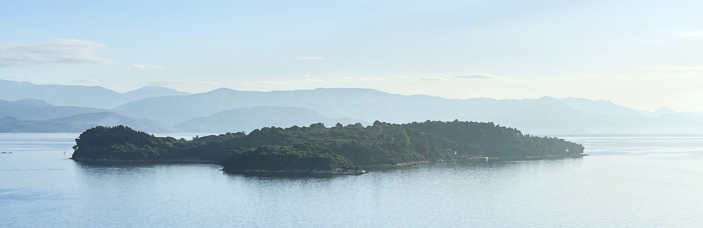 Isola boscosa in acque calme davanti a una catena montuosa